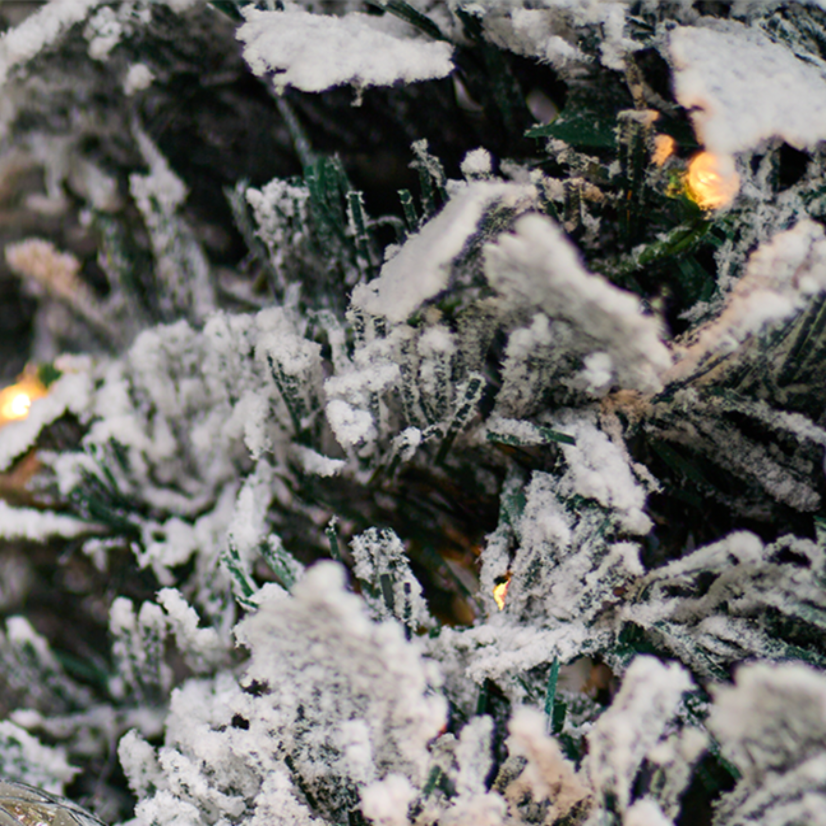Gros plan sur les branches enneigées d’un sapin de Noël artificiel, illuminées par de petites lumières LED blanc chaud, Maison Eira.
