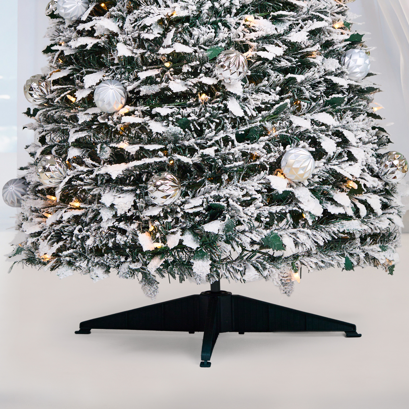 Bas d’un sapin de Noël artificiel pliable enneigé avec boules argentées, lumières LED blanc chaud et trépied en PVC vert foncé élégant, Maison Eira